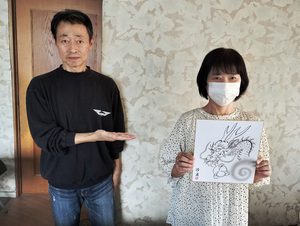 水墨龍画教室の体験イメージ。講師が龍画の作品を紹介し、隣の人が完成見本の色紙を持っている様子